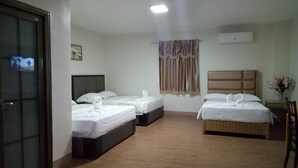 A hotel room with two beds, a wooden floor, a window with curtains, a wall-mounted air conditioner, and a door with a glass panel. - Meaco Royal Hotel - Batangas City (Batangas City)