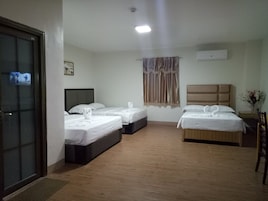 Quarto de hotel com duas camas, piso de madeira, janela com cortinas, ar-condicionado fixado na parede e porta com painel de vidro.