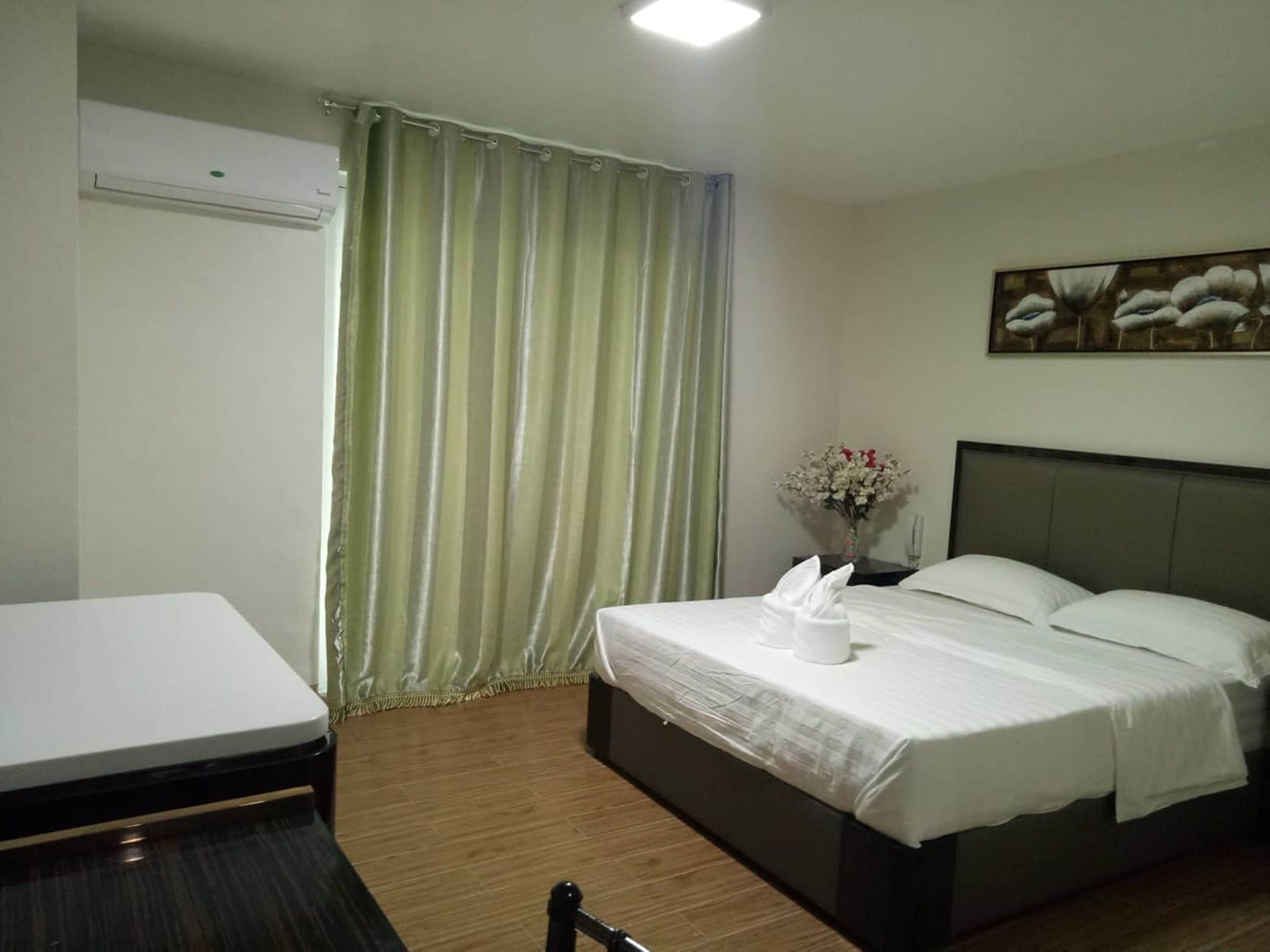 A hotel room with a bed, a bedside table with a vase of flowers, a chair, and a desk with a chair.
