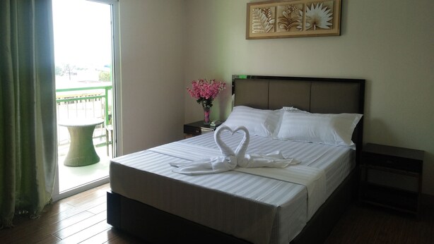A hotel room with a bed, a nightstand, a vase with flowers, a window with curtains, and a wall art piece. - Meaco Royal Hotel - Batangas City (Batangas City)