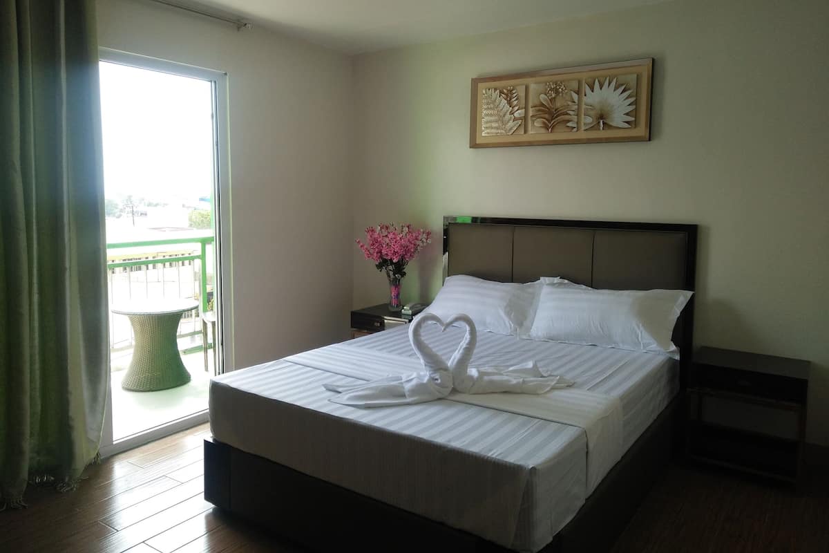 A hotel room with a bed, a nightstand, a vase with flowers, a window with curtains, and a wall art piece.
