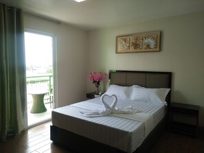 Una habitación de hotel con cama, mesita de noche, un florero con flores, ventana con cortinas y una obra de arte en la pared.