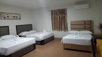 Habitación de hotel con tres camas, cada una con ropa de cama blanca y toallas con forma de cisne decorativas. Hay un cuadro en la pared, una ventana con cortinas y un equipo de aire acondicionado también en la pared.