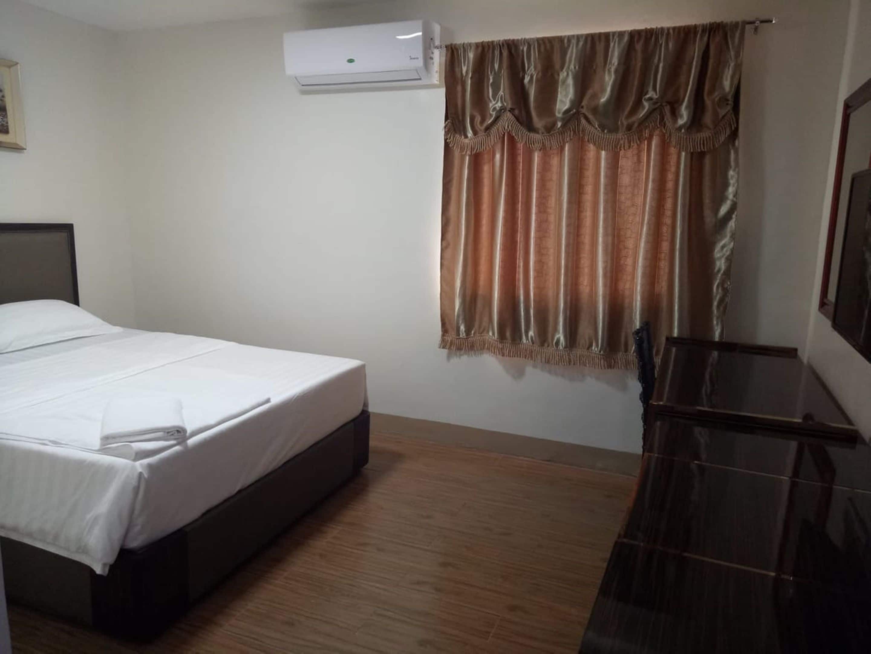 A hotel room with a bed, a desk, and an air conditioning unit.