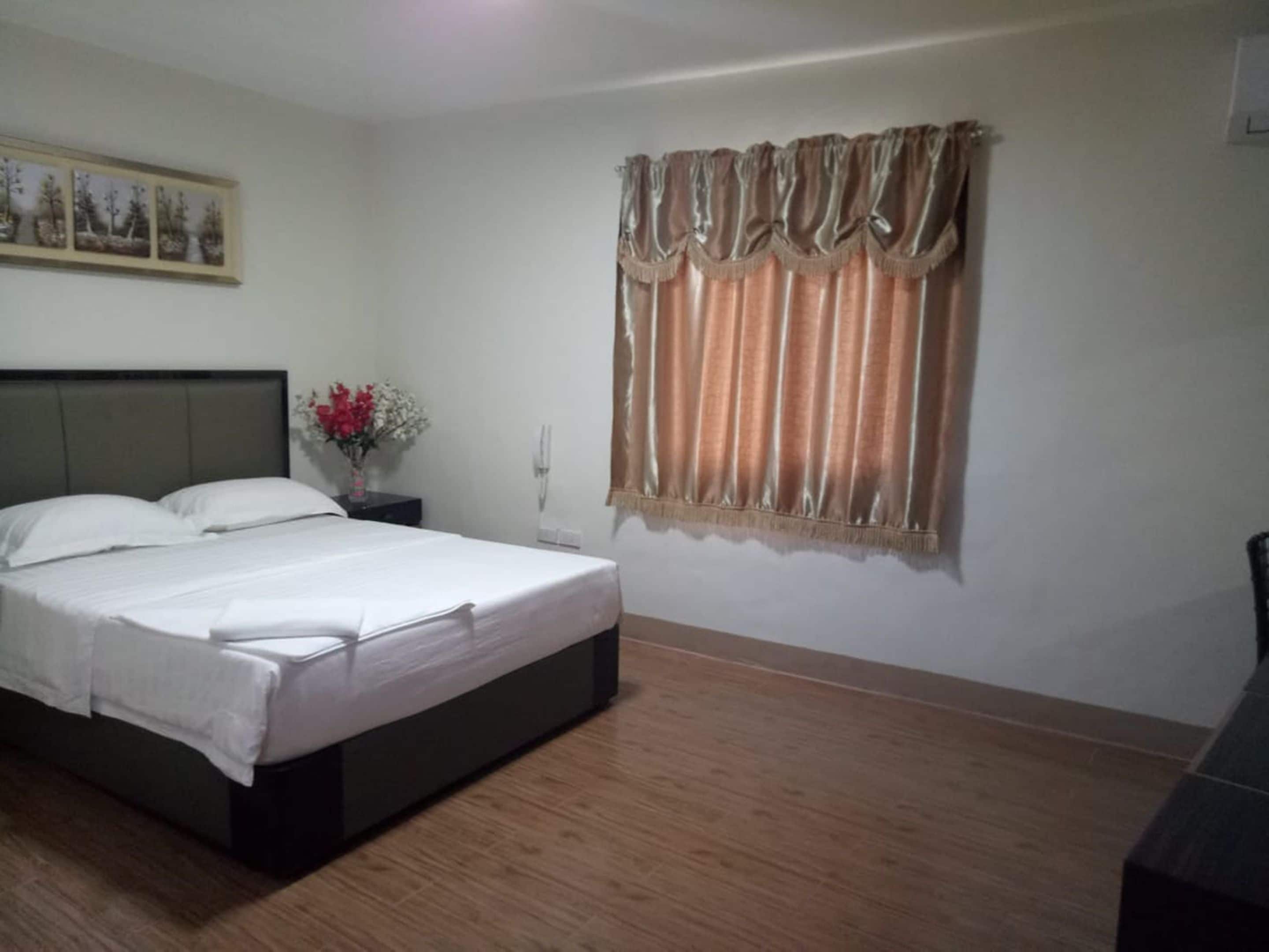 A bedroom with a bed, a nightstand with a vase of flowers, and a window with curtains.