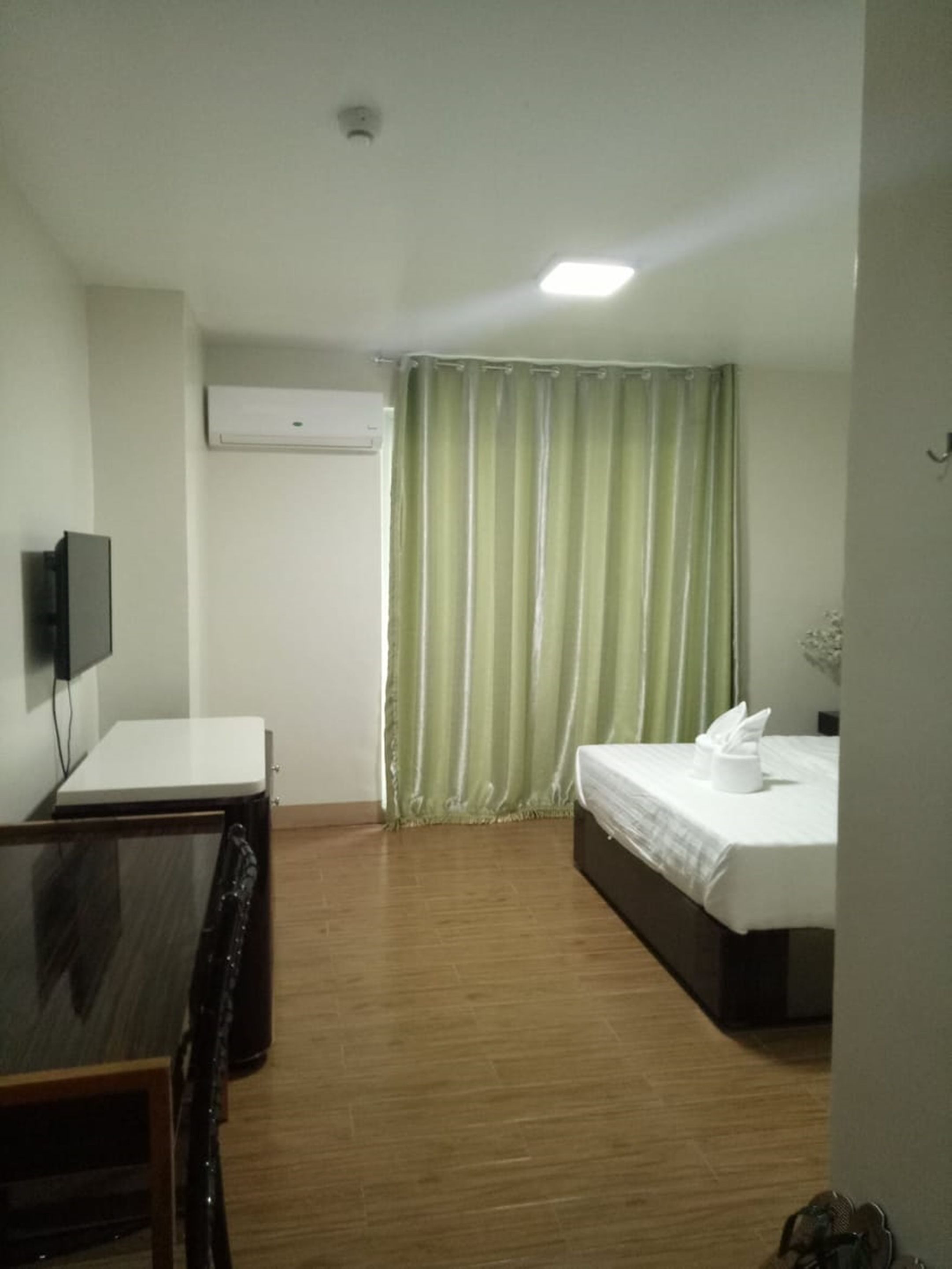 A hotel room with a bed, a desk, a chair, an air conditioning unit, and a window with curtains.