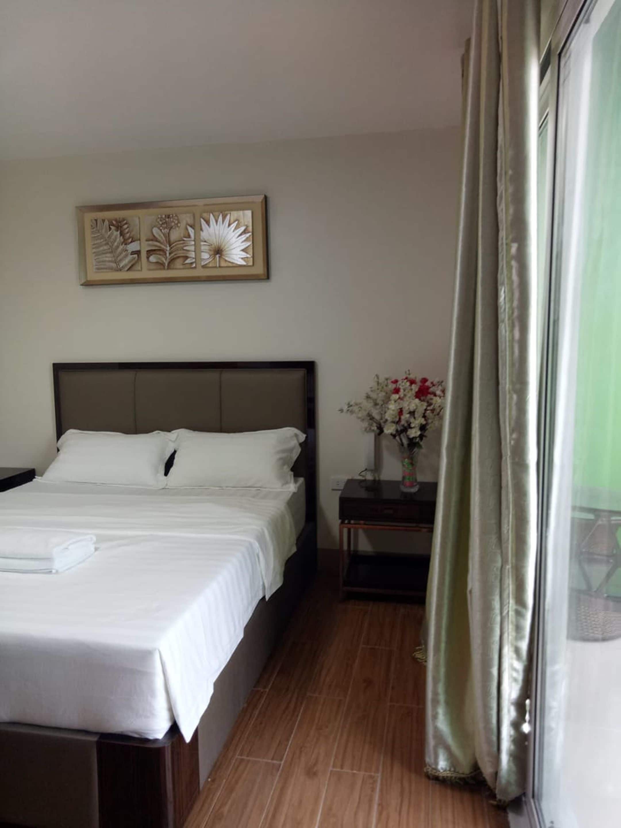 A neatly made bed with white linens, a bedside table with a vase of flowers, and a wall-mounted decorative piece above the bed.