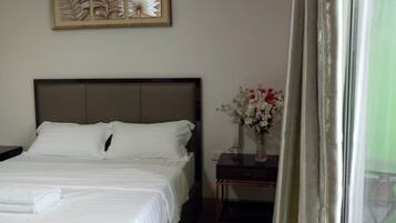 A neatly made bed with white linens, a bedside table with a vase of flowers, and a wall-mounted decorative piece above the bed.