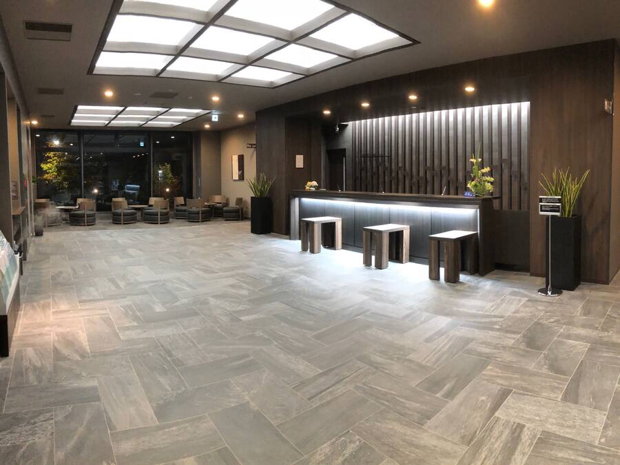Een moderne receptiebalie met een visgraatvloer, een receptiemedewerker en zithoekjes.