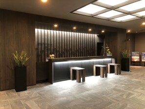 Una moderna reception con top in legno scuro, un divisorio in vetro e una pianta in vaso a sinistra.