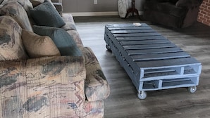 Een woonkamer met een gestreept bankje, een donkere fauteuil en een metalen karretje.