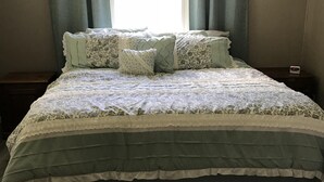 Een slaapkamer met een groot bed, meerdere kussens, een nachtkastje, een klok en een raam met gordijnen.