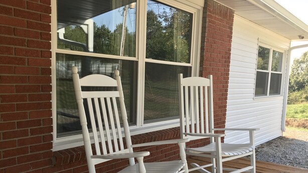 Een veranda met twee witte schommelstoelen en een bakstenen muur.