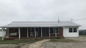 Een gelijkvloers huis met een veranda, een schommel en een kleine schuur.