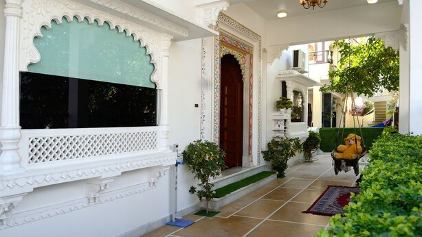 A traditional building with ornate white architectural details, a red door, and a hanging swing chair. - Ambay Villa (Udaipur)