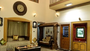 A traditional room with a bed, a wooden bench, a mirror, and a wall clock. - Ambay Villa (Udaipur)
