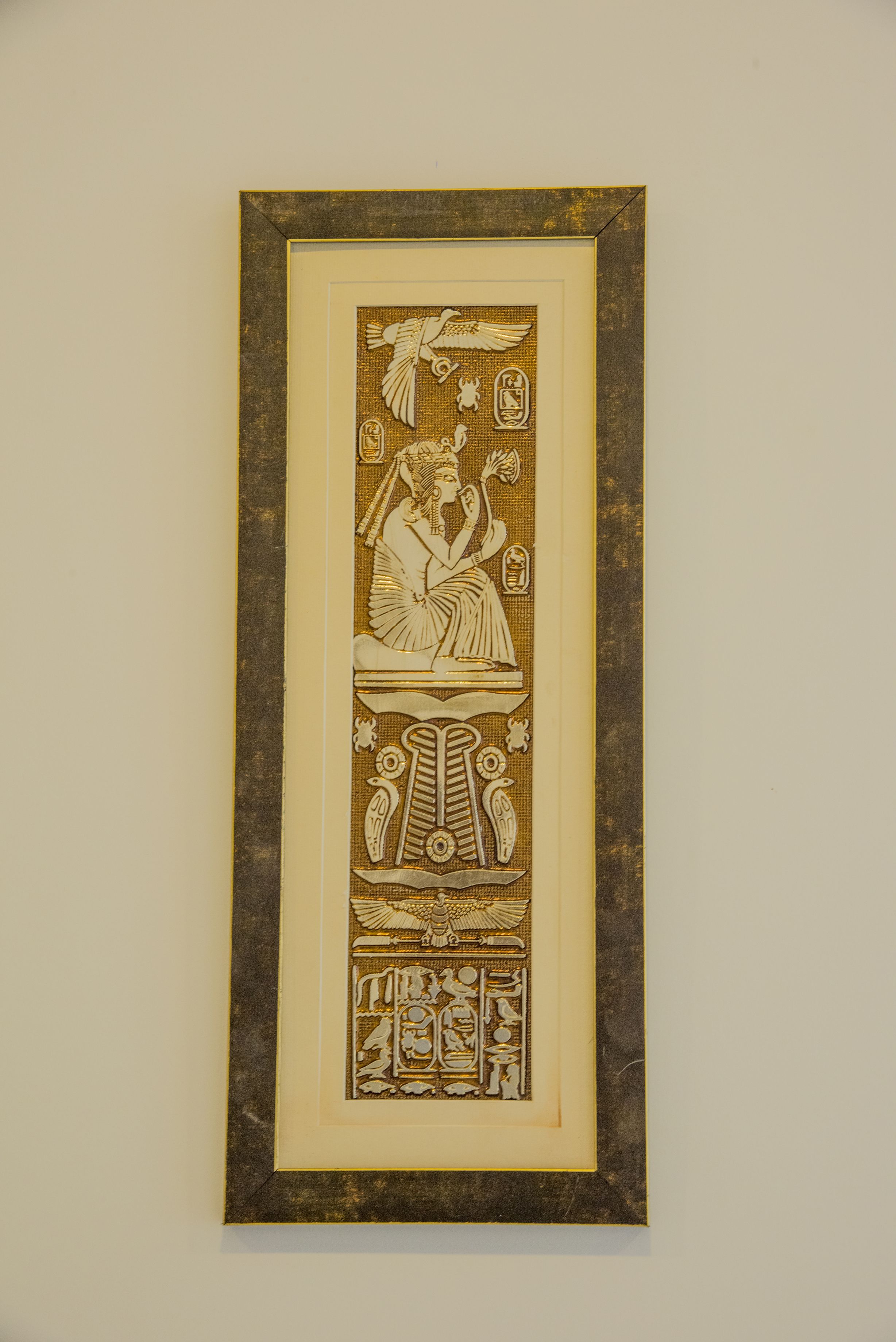A framed ancient Egyptian artifact with hieroglyphics and a seated figure.