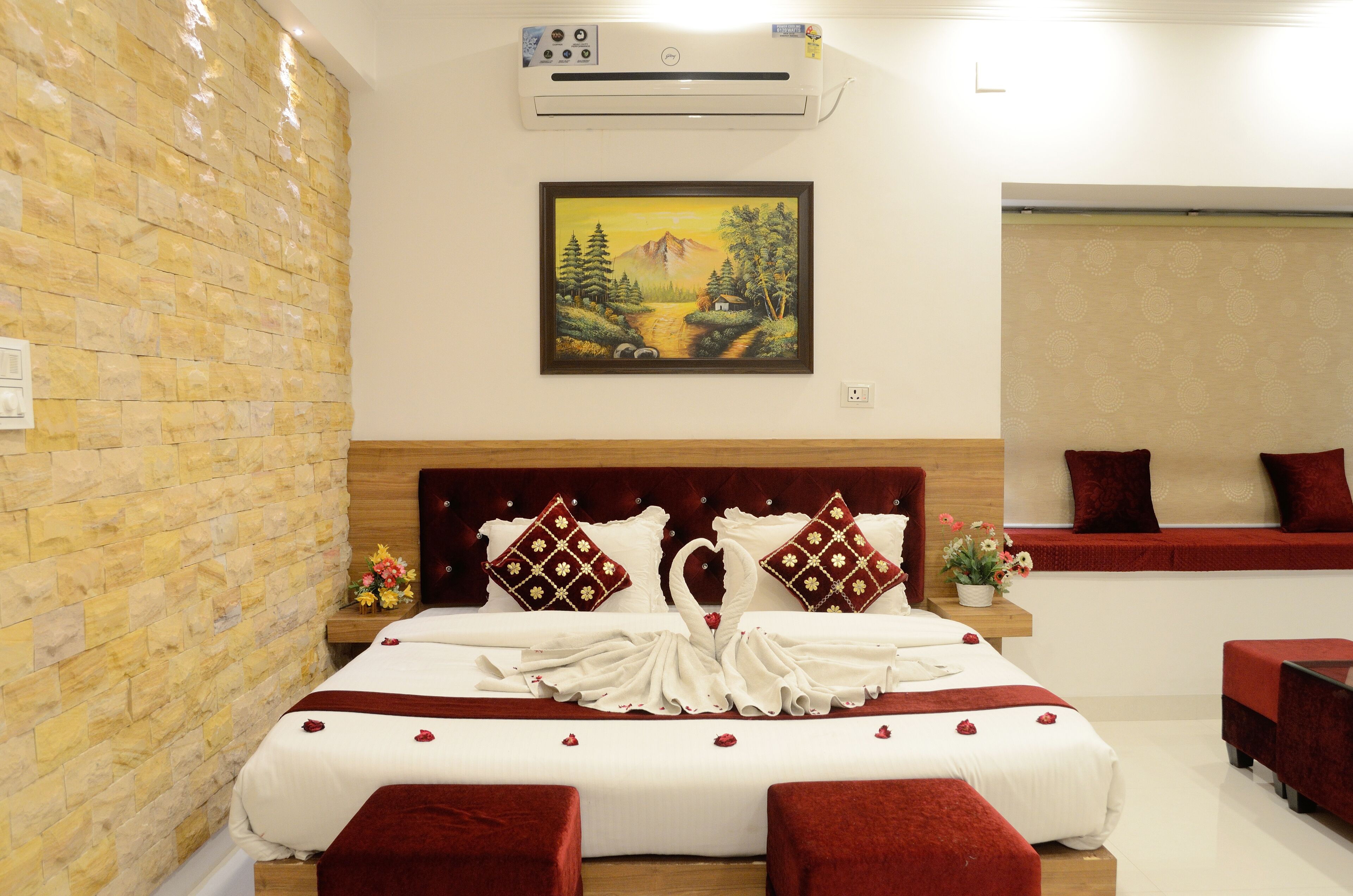 Una habitación de hotel con pared de piedra, cama con ropa de cama roja y blanca, un cuadro de un paisaje y un sofá rojo.