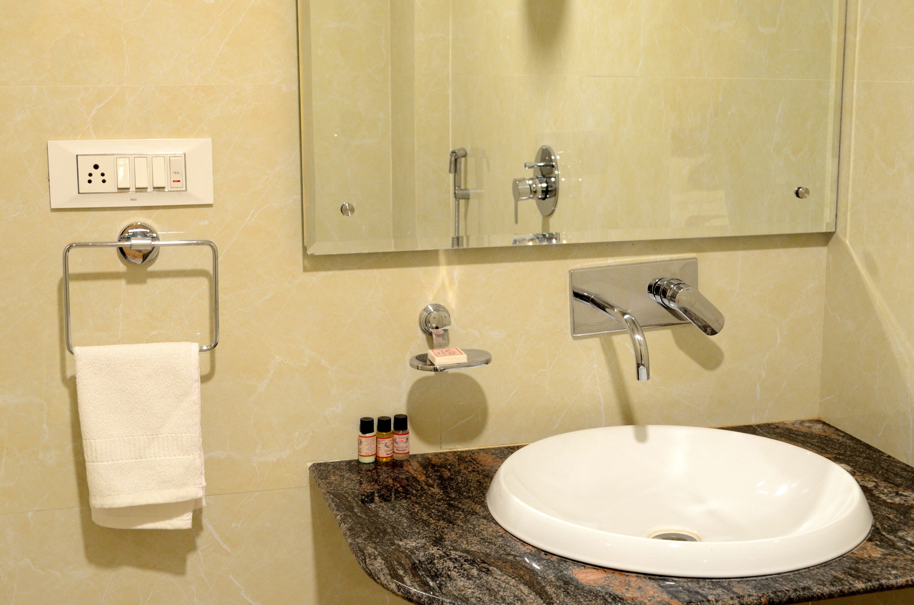 A bathroom with a white sink, a mirror, a towel rack, a soap dispenser, and a power outlet.