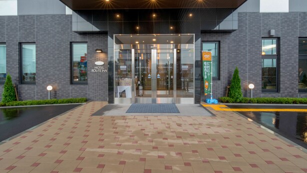 Een moderne hotelentree met een glazen deur, een overdekte doorgang en een betegeld voetpad.