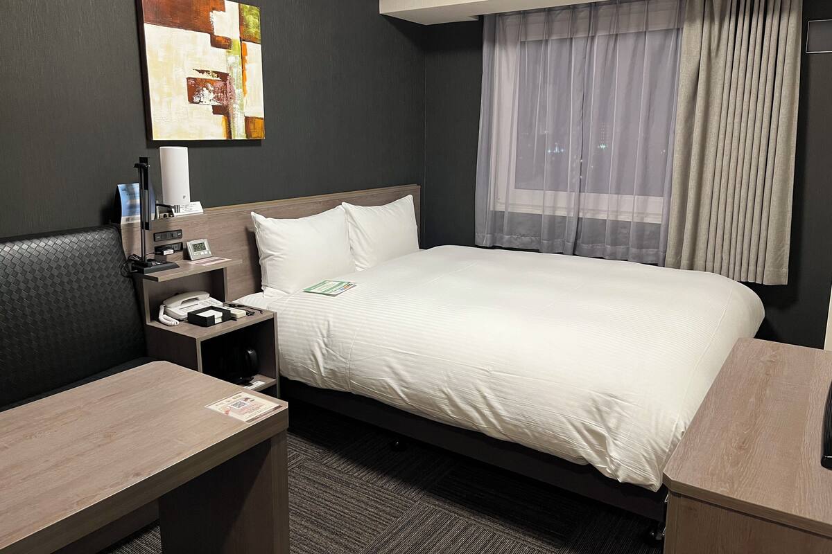 Una habitación de hotel con cama, mesita de noche, lámpara y un cuadro en la pared.