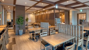 Een modern restaurant met houten tafels en stoelen, een potplant en een houten scheidingswand.
