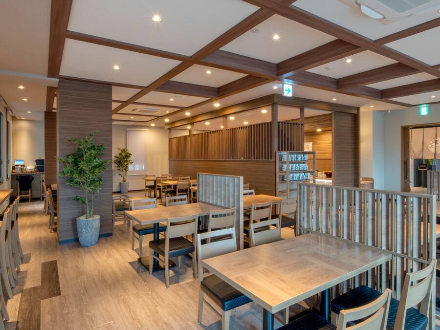A modern restaurant with wooden tables and chairs, a potted plant, and a wooden partition.