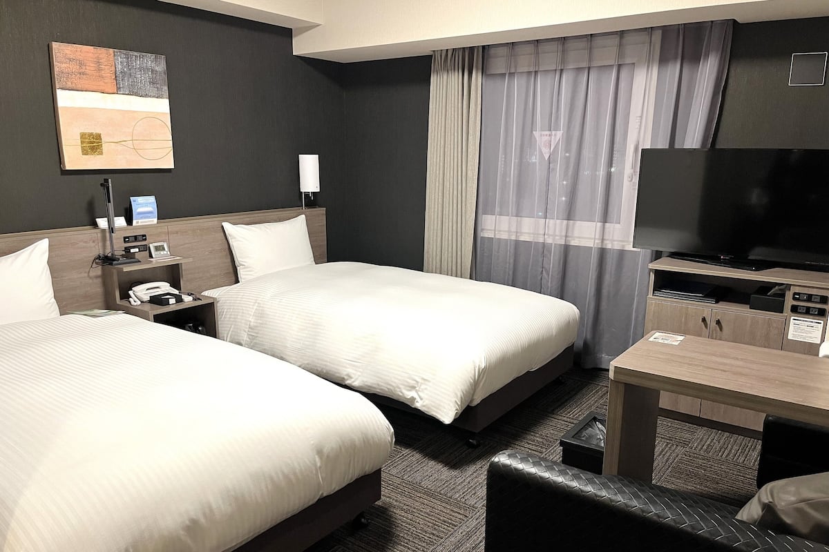 Una habitación de hotel con dos camas, un escritorio, un televisor y un cuadro en la pared.
