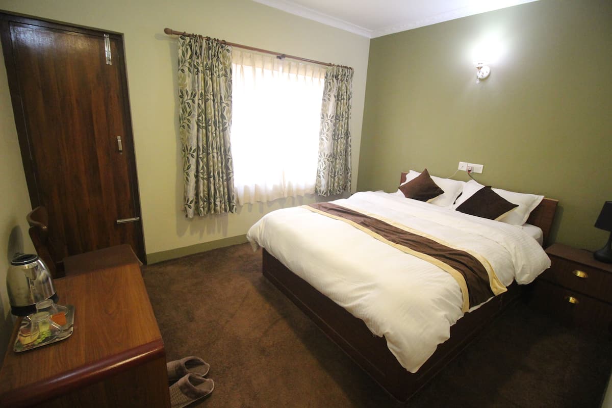 A bedroom with a bed, a desk, a chair, a window with curtains, and a nightstand.