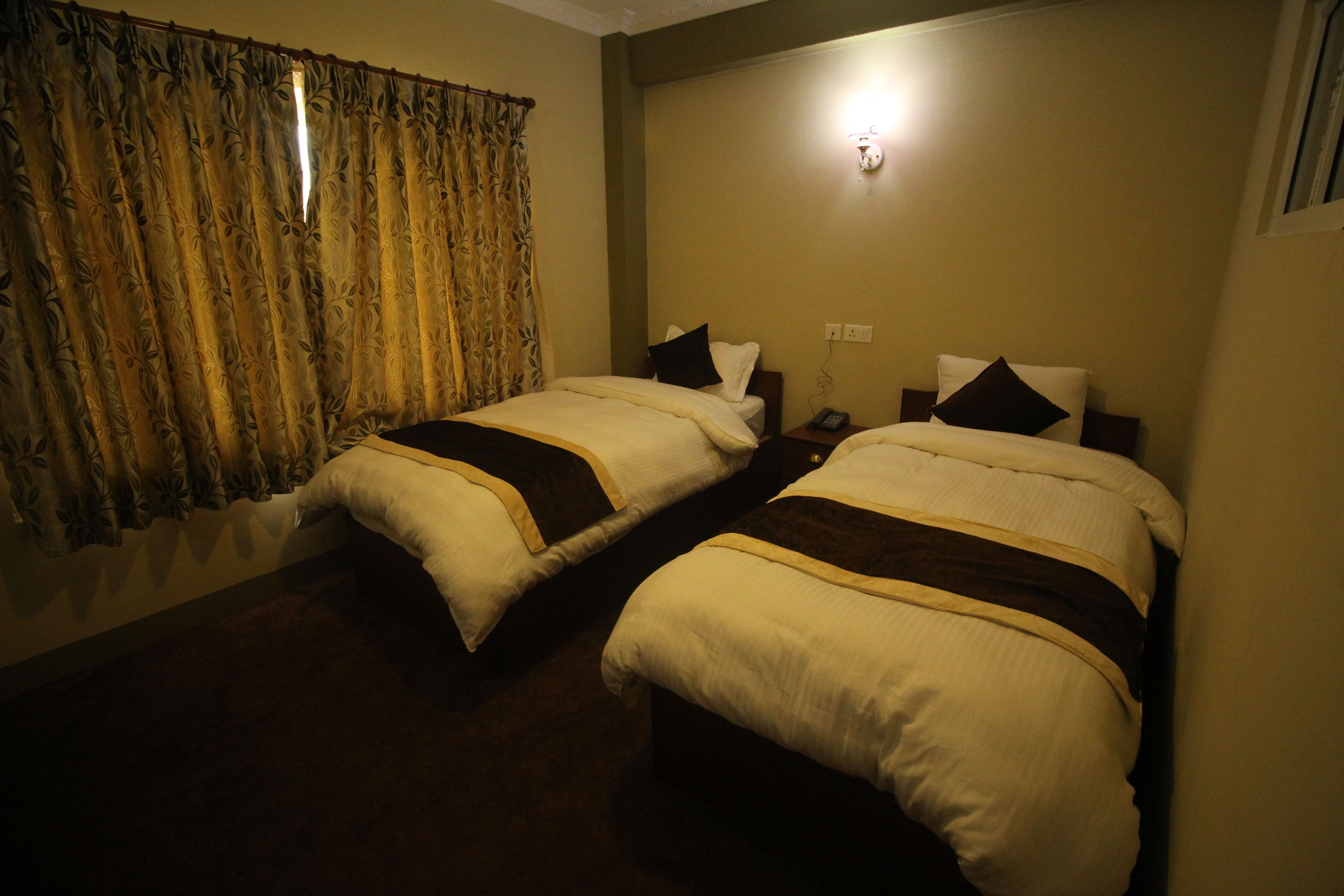 Una habitación de hotel con dos camas individuales, una mesita de noche con lámpara y una cortina con estampado floral.