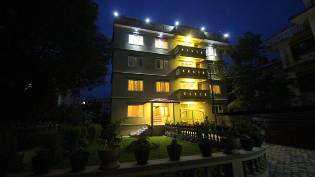 Un hôtel à plusieurs étages, doté de fenêtres illuminées et d’un jardin bien entretenu.