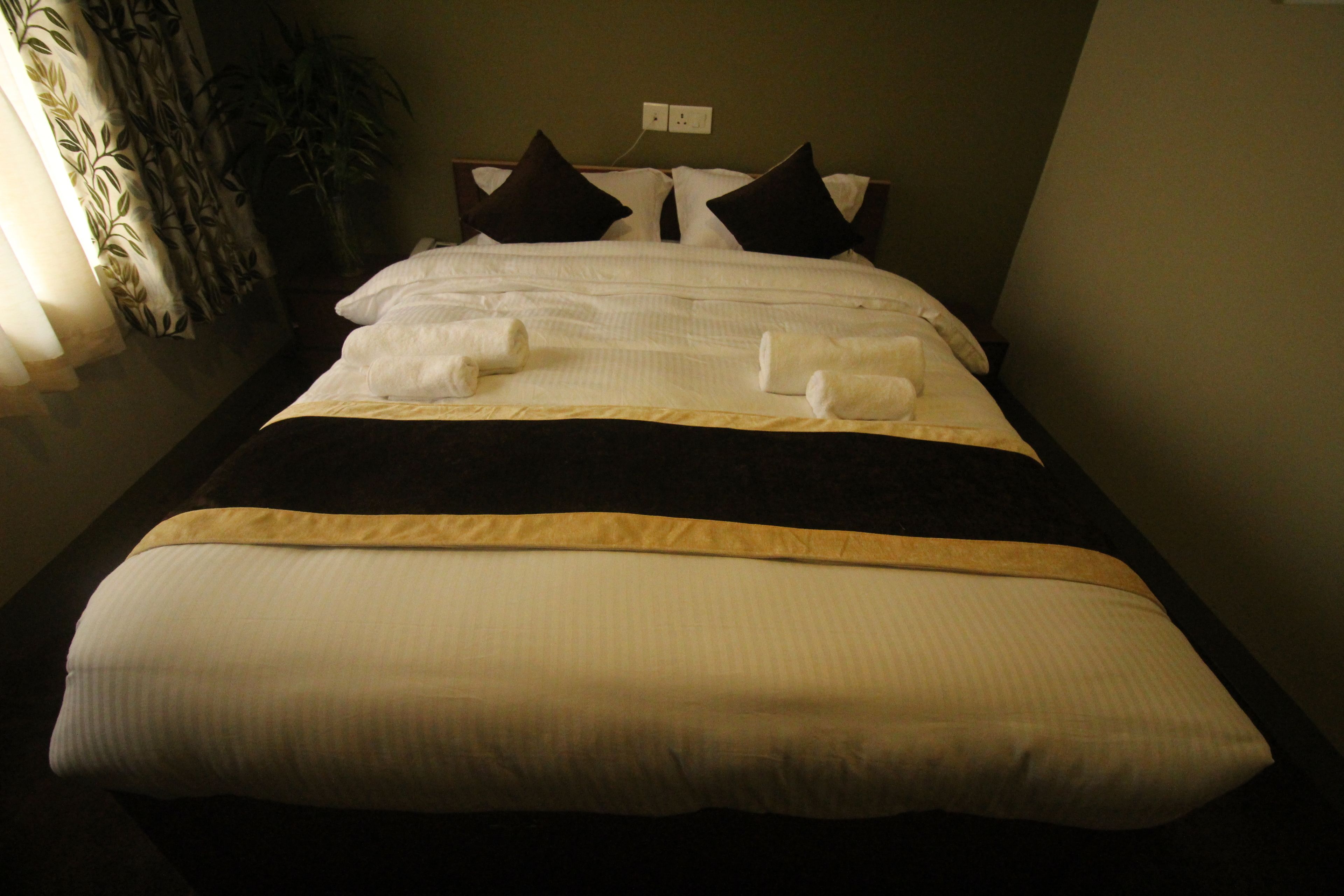 A neatly made bed with white and brown bedding, a dark headboard, and a power outlet on the wall.