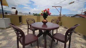 Une table ronde, quatre chaises et un vase de fleurs sur une terrasse carrelée.
