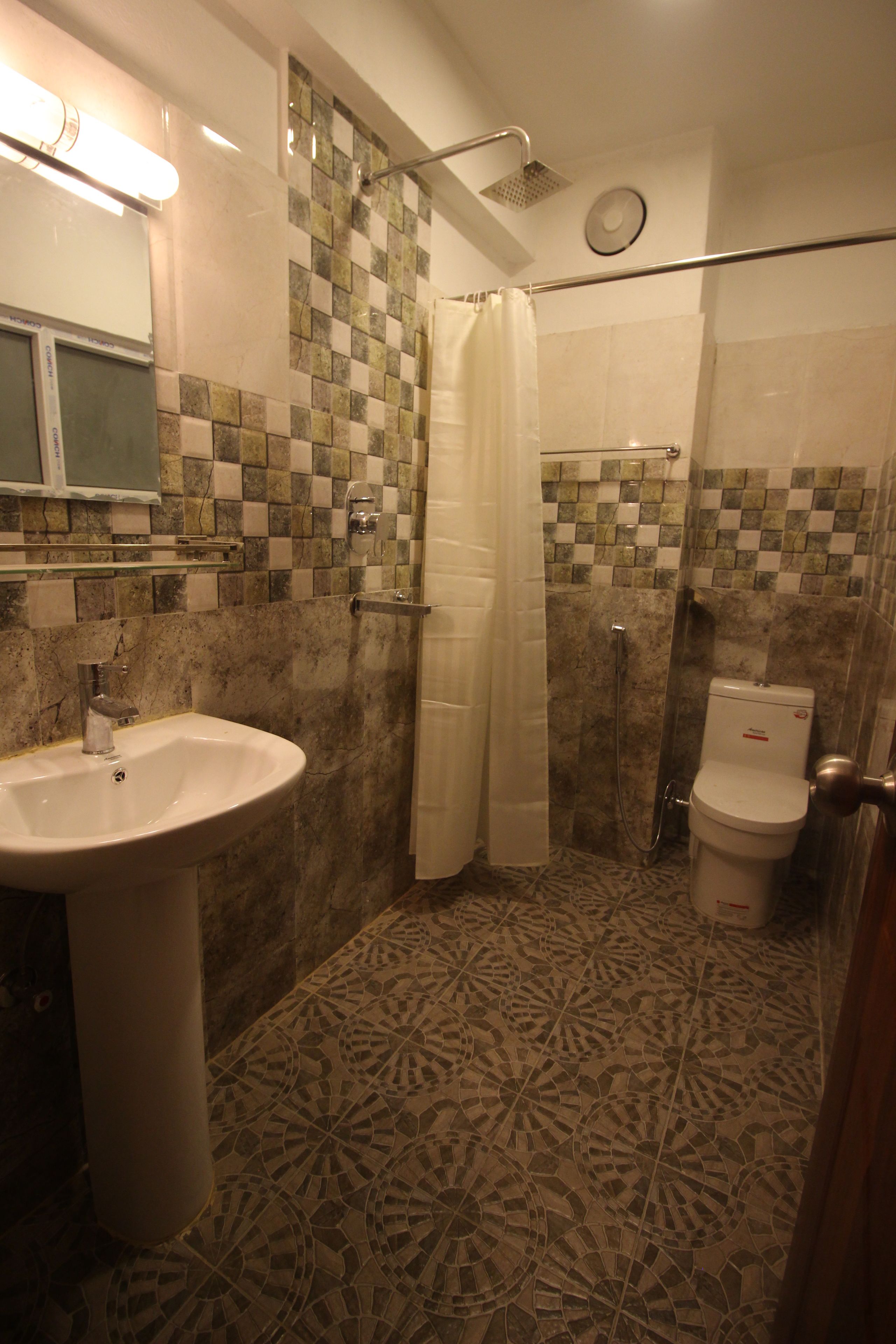 A bathroom with a sink, toilet, shower, and patterned floor tiles.