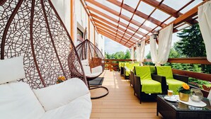 Un espacio de estar al aire libre techado con mobiliario de mimbre, una silla colgante y una terraza de madera.
