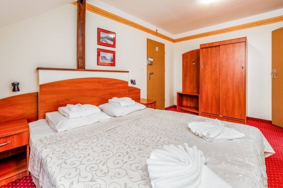 A hotel room with a wooden headboard, a large bed with white linens, a wooden wardrobe, and a red carpet.