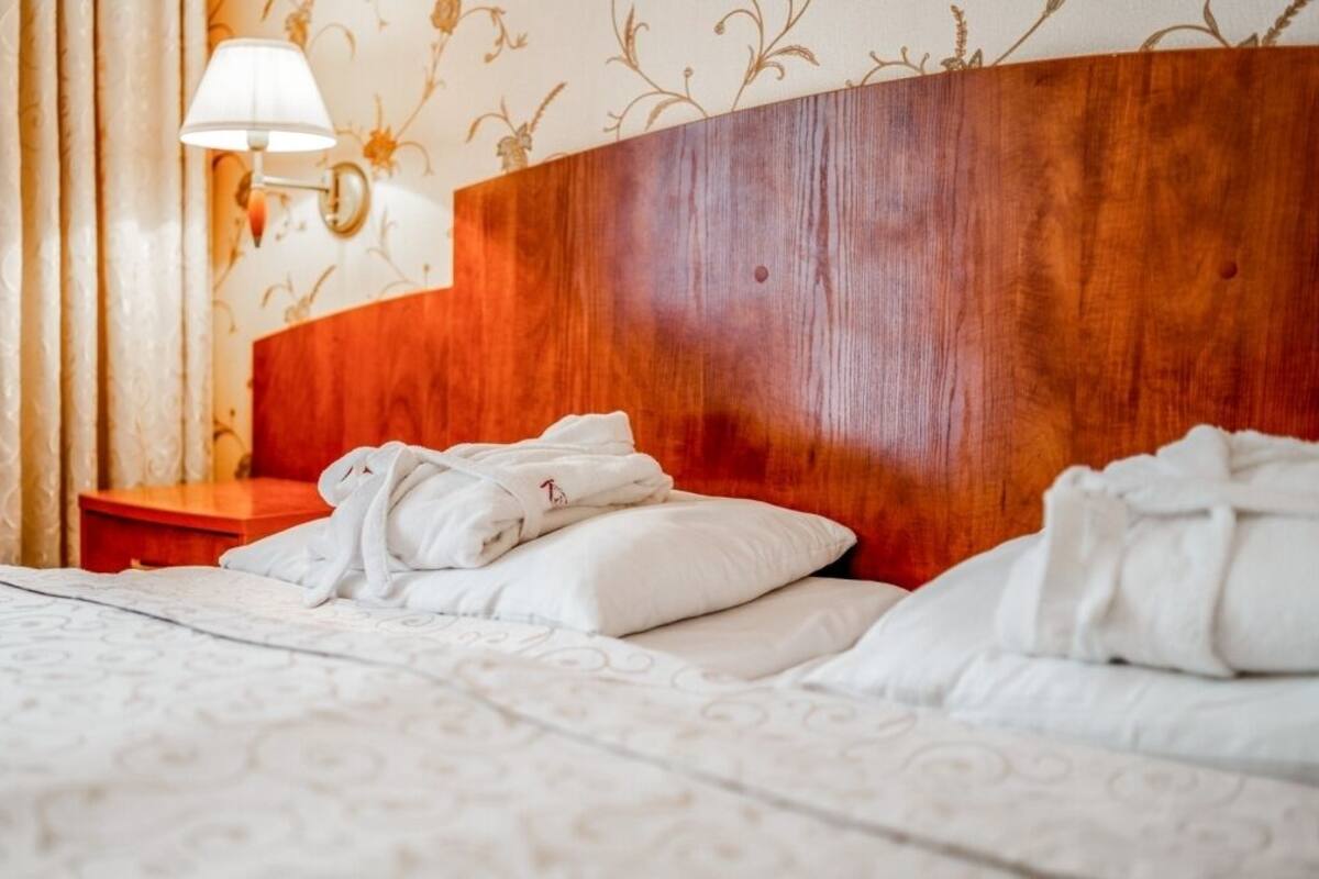 A hotel room with a wooden headboard, a bedside table with a lamp, and neatly folded towels on the bed.