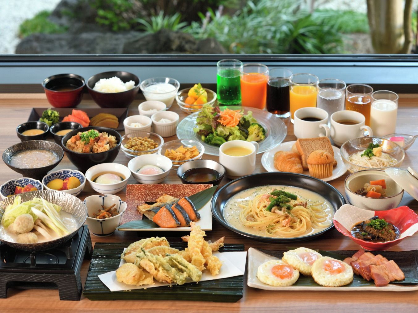 Ett urval av japanska rätter och drycker står uppdukat på ett bord med utsikt över grönskan utanför.