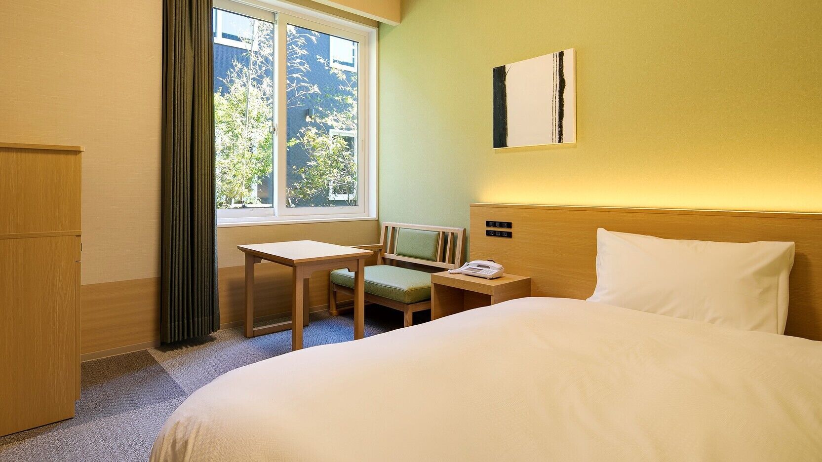 Une chambre d’hôtel avec un lit, un bureau, une chaise, un téléphone et une fenêtre avec des rideaux.