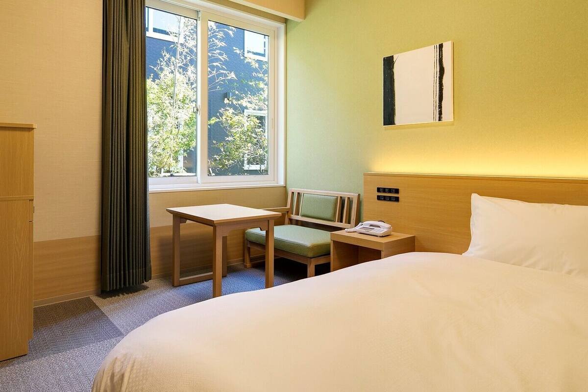 Habitación de hotel con cama, escritorio, silla, teléfono y ventana con cortinas.