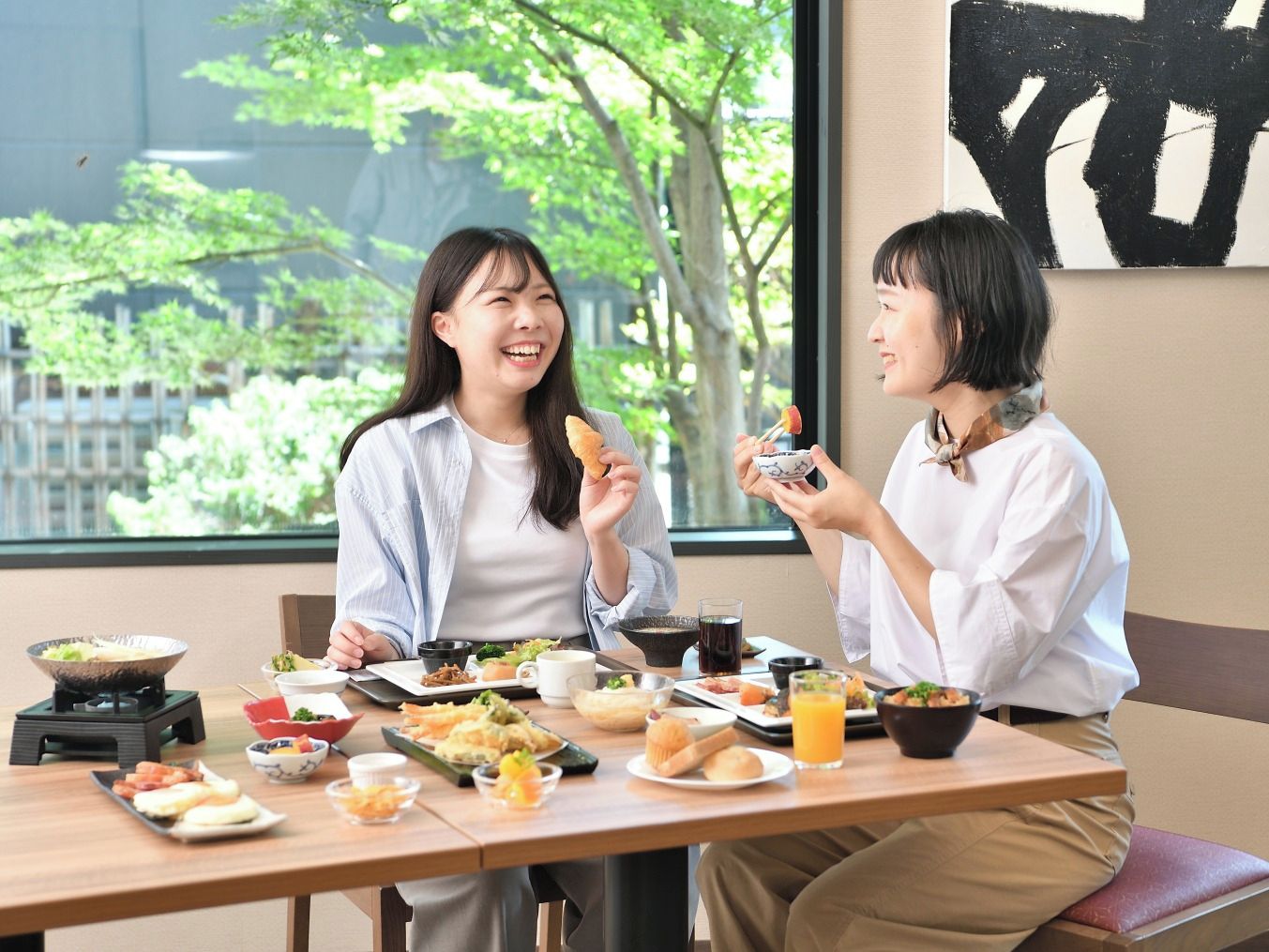 Dos personas cenando en una mesa con varios platos, un fogón caliente y vistas a árboles afuera.