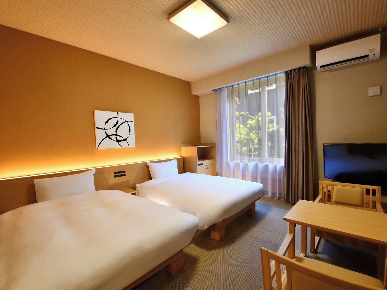 A hotel room with two beds, a desk, a television, and an air conditioning unit.