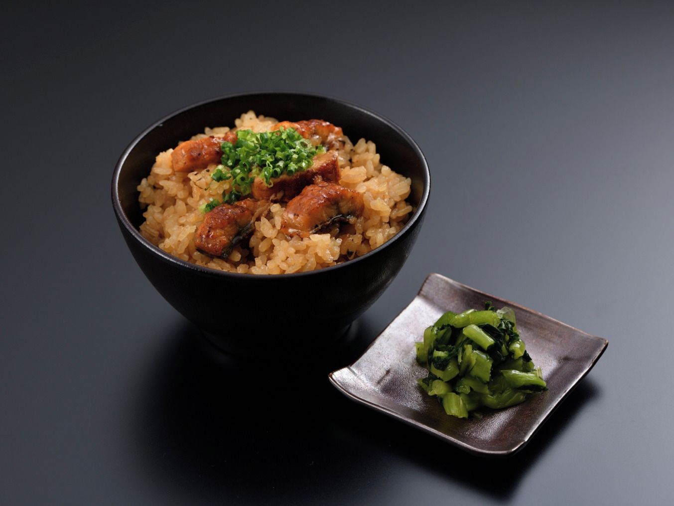 A bowl of rice with meat and green garnish on a dark surface.