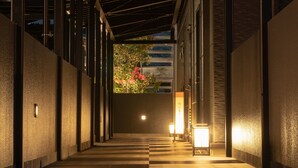 A corridor with a wooden floor and metal beams, leading to a brightly lit entrance. - Grandvrio Hotel Nara Wakura (Tenri)