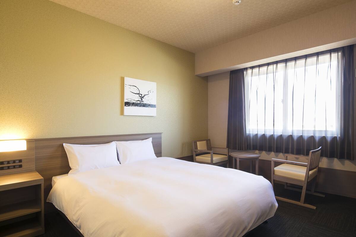 Una habitación de hotel con una cama, una silla, una mesita y una ventana con cortinas.