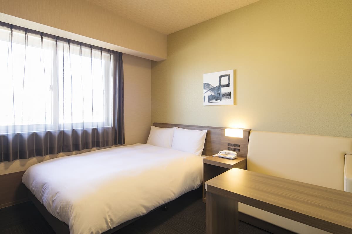 Una habitación de hotel con cama, mesita de noche, lámpara y un cuadro en la pared.
