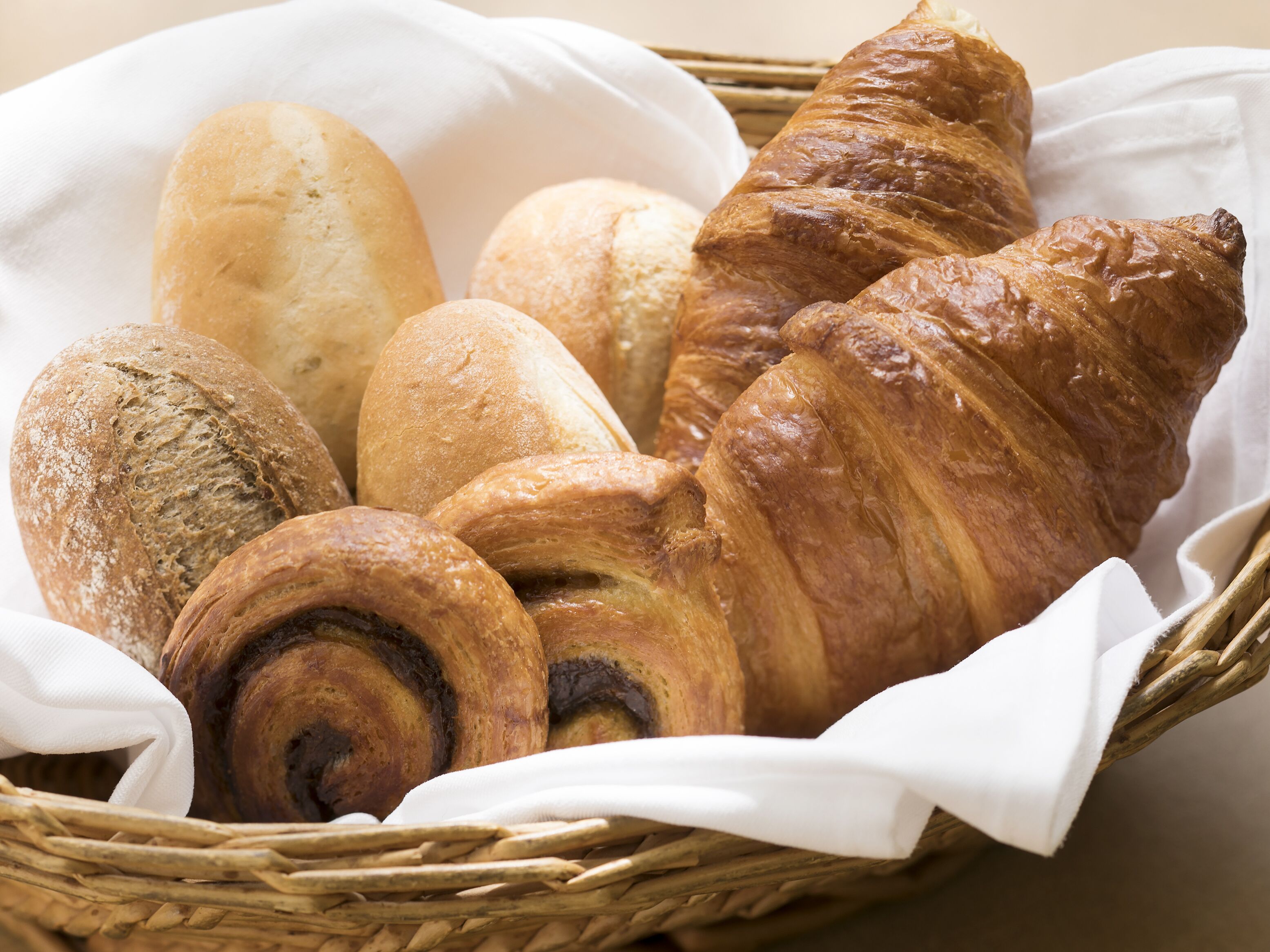 Un panier contenant divers types de pain, notamment des croissants, une baguette et des petits pains.