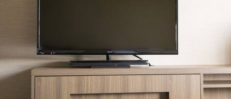 A flat-screen TV on a wooden cabinet with a control panel and a booklet.
