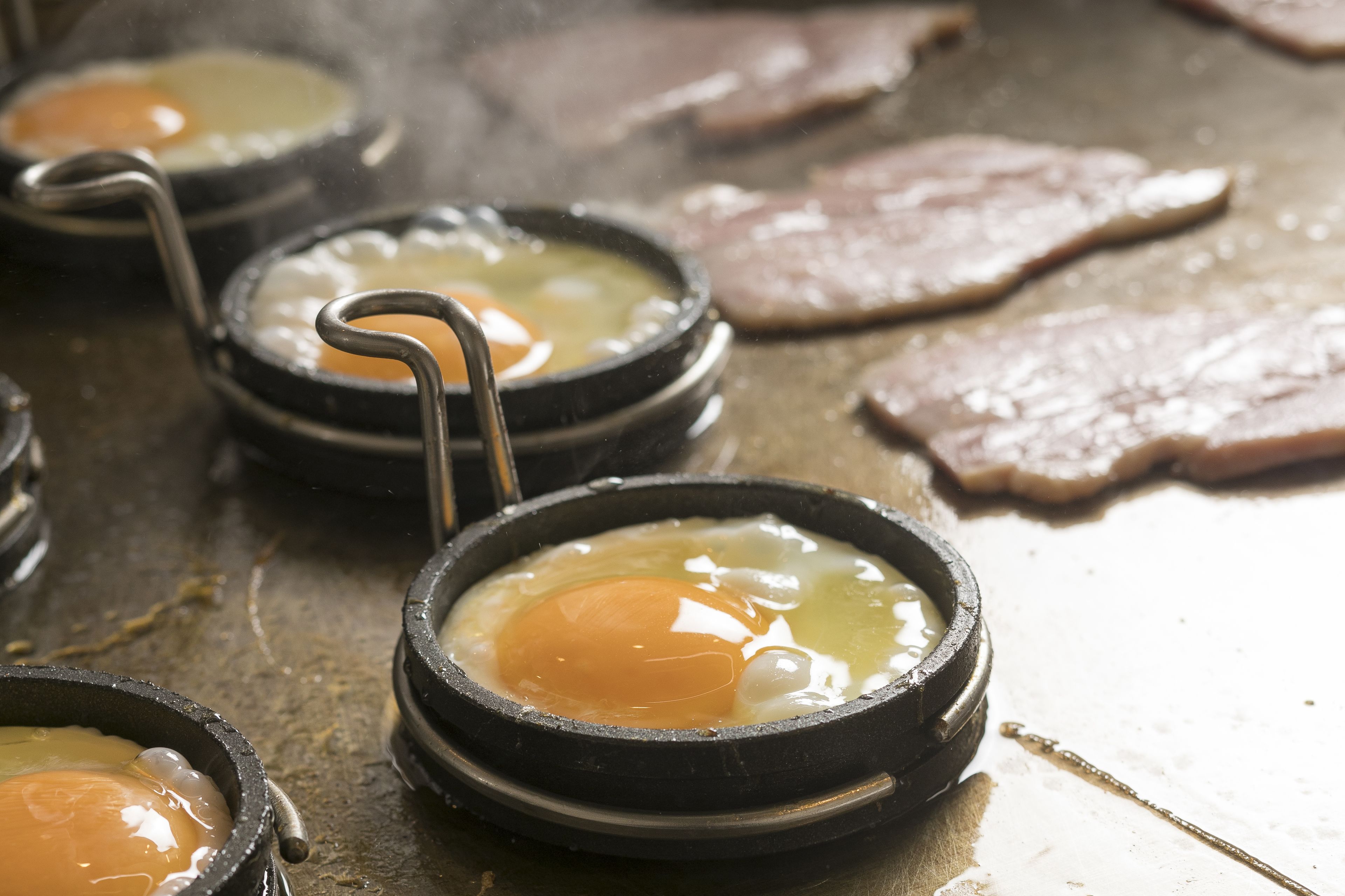 Una preparación para cocinar con varias ollas negras pequeñas que contienen huevos en una superficie plana.