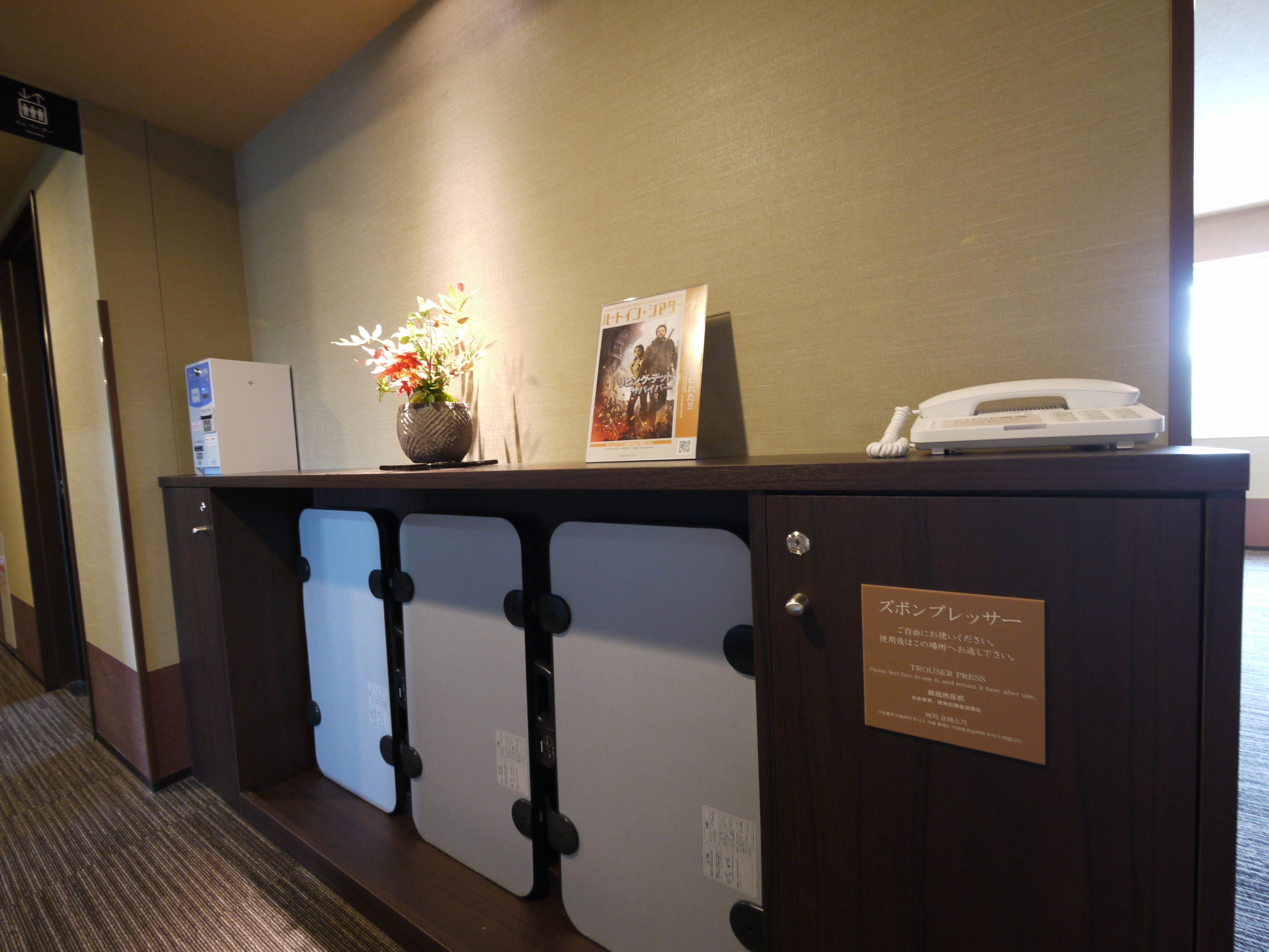 A reception desk with a vase of flowers, a poster, a phone, and a sign with Japanese text.